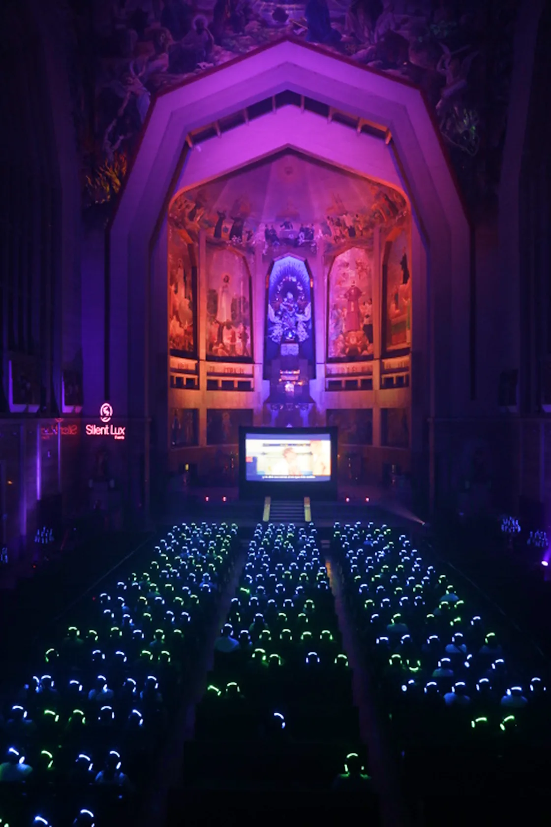 La nave de la parroquia llena de asistentes con audífonos luminosos encendidos